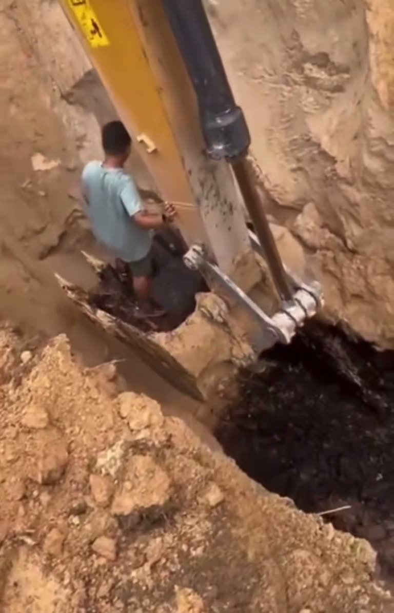 Worker Rides Excavator Bucket Into Deep Pit as Crew Shouts Warning