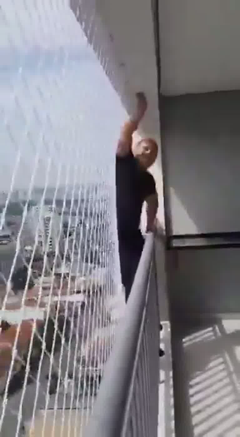 Man Climbs Over High-Rise Balcony Railing Beside Safety Net